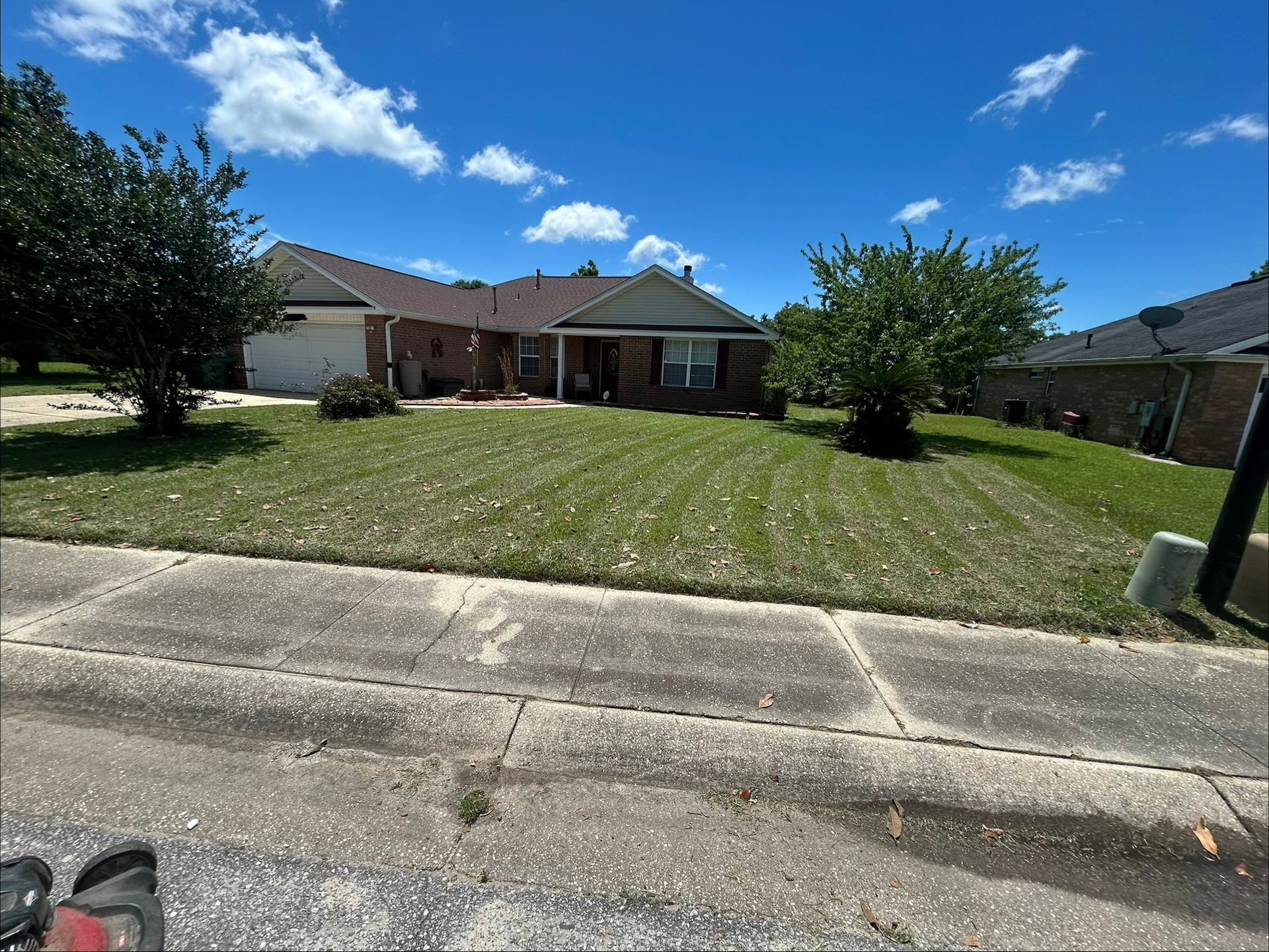 Single-story brick house with manicured lawn and driveway on a sunny day with blue sky