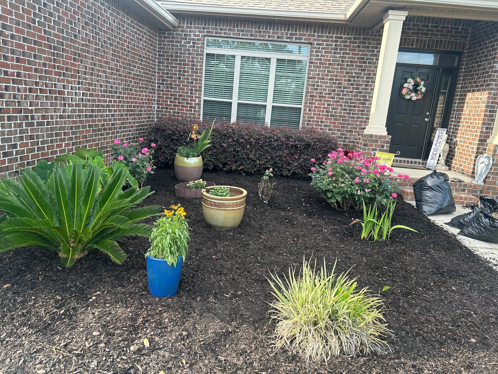 Front entrance landscaping with flowering shrubs, ornamental grasses, and potted plants against a brick home facade